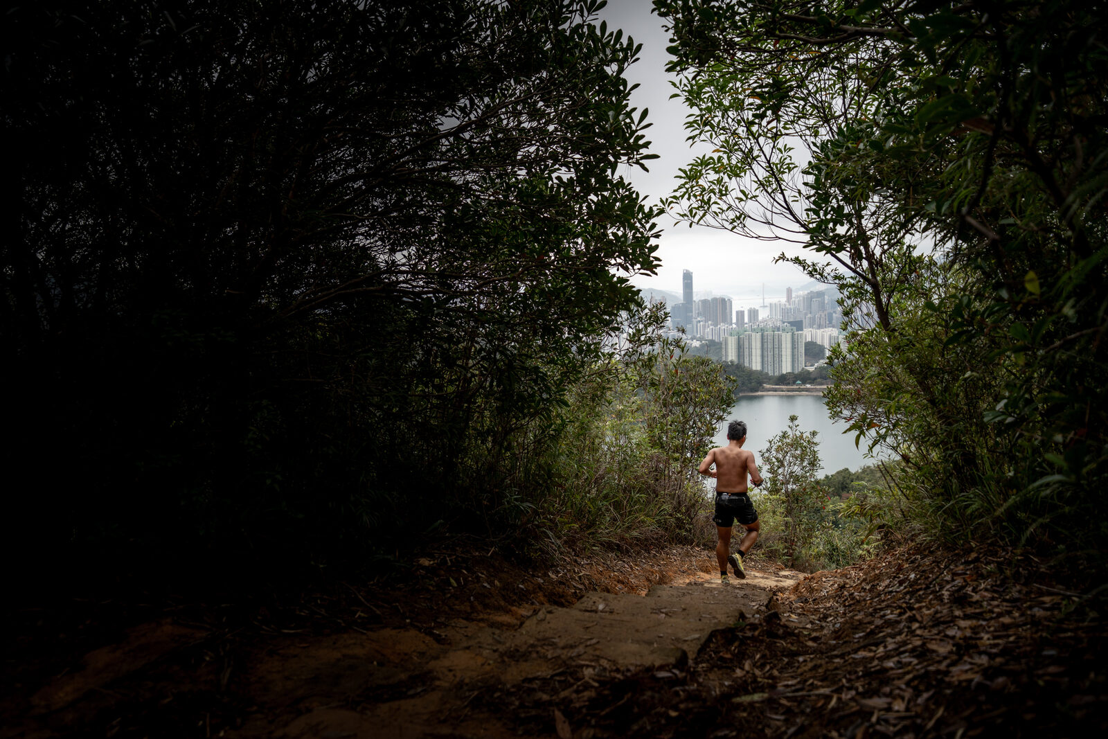 Runner descending a trail toward the city and reservoir
