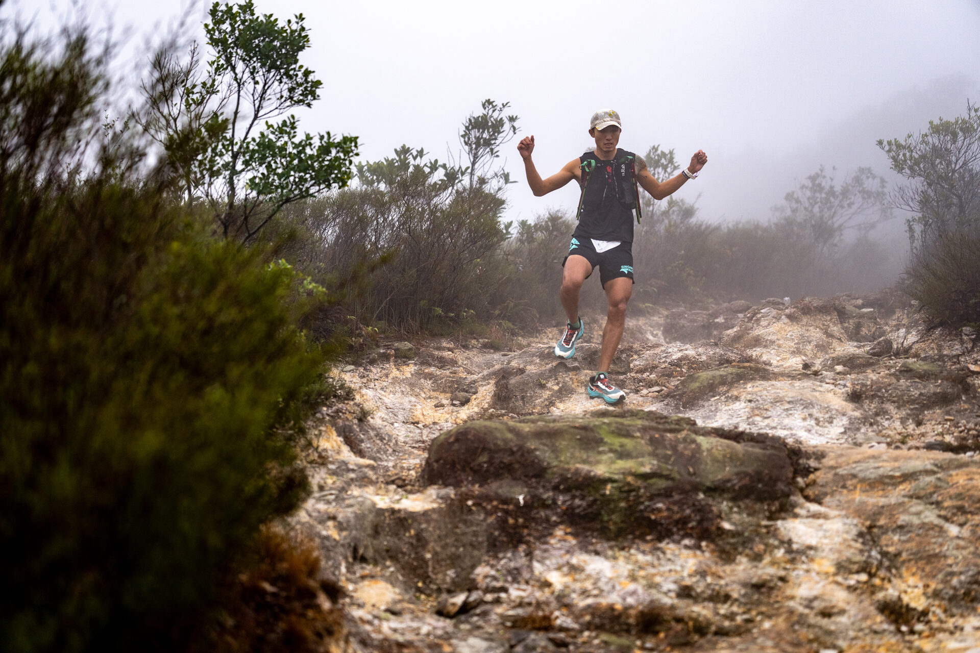 Runner with arms raised on a misty rocky summit
